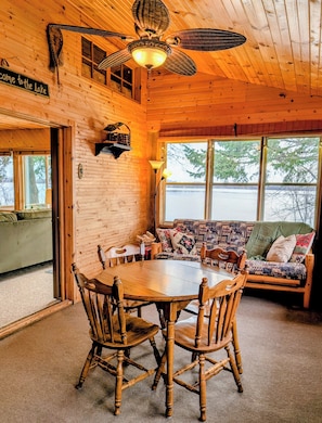 A wooden cabin interior with a dining table, chairs, a sofa, and a ceiling fan.