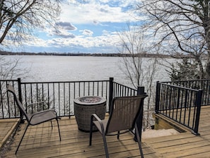 A wooden deck with two chairs and a round table, overlooking a frozen lake.