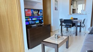 Ein Wohnzimmer mit Flachbildfernseher, Holzschrank, Couchtisch, Essbereich mit Stühlen und einer Couch.