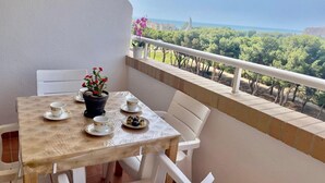 Ein Balkon mit einem Tisch für zwei Personen, einem Blumentopf und Blick auf eine Küstenlandschaft.
