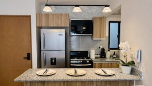 Une cuisine moderne équipée d’un réfrigérateur, d’un four et d’un micro-ondes encastrés. Elle comprend des plans de travail en granit et un coin repas avec des chaises.