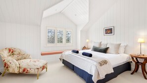 A bedroom with a bed, a chair, a bedside table, a lamp, and a window with blinds. - Mulgrave House & Cottage (Bellawongarah)