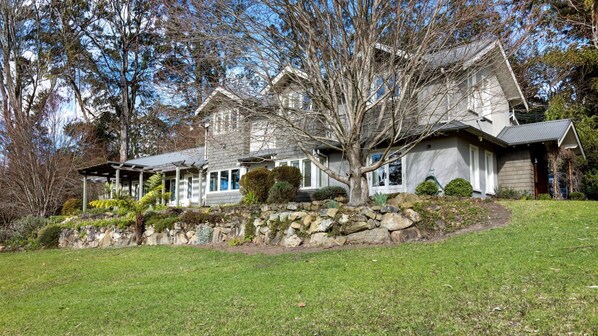A two-story house with a stone retaining wall, a covered patio, and a well-maintained lawn. - Mulgrave House & Cottage (Bellawongarah)