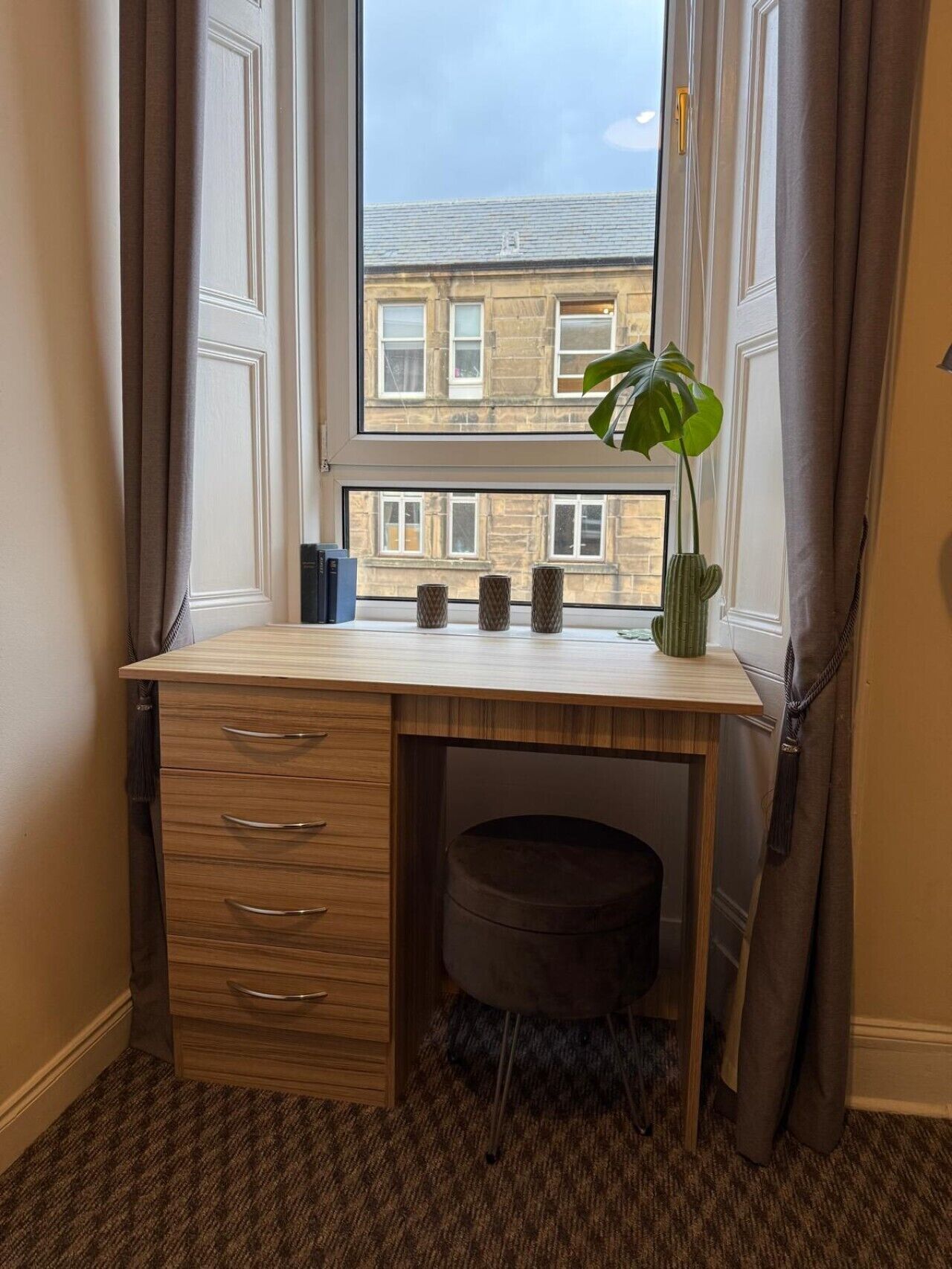 A corner room with a desk, a window, and a view of buildings.