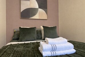 Una cama bien hecha con almohadas, una toalla doblada y una manta.