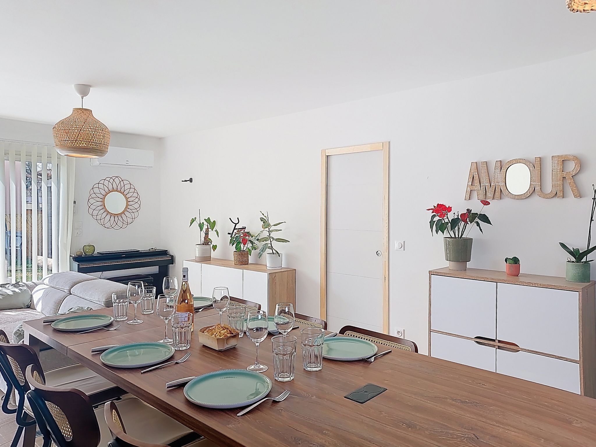 A dining area with a wooden table set for four, a piano, and a mirror on the wall.