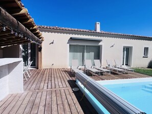 Ein Poolbereich mit Liegestühlen, einer Holzterrasse und einem Gebäude mit einem Ziegeldach.
