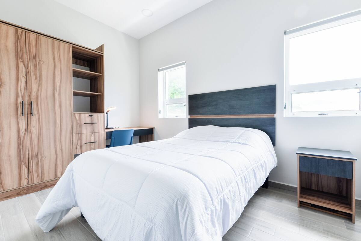 A bedroom with a bed, a wardrobe, a desk, and a window.