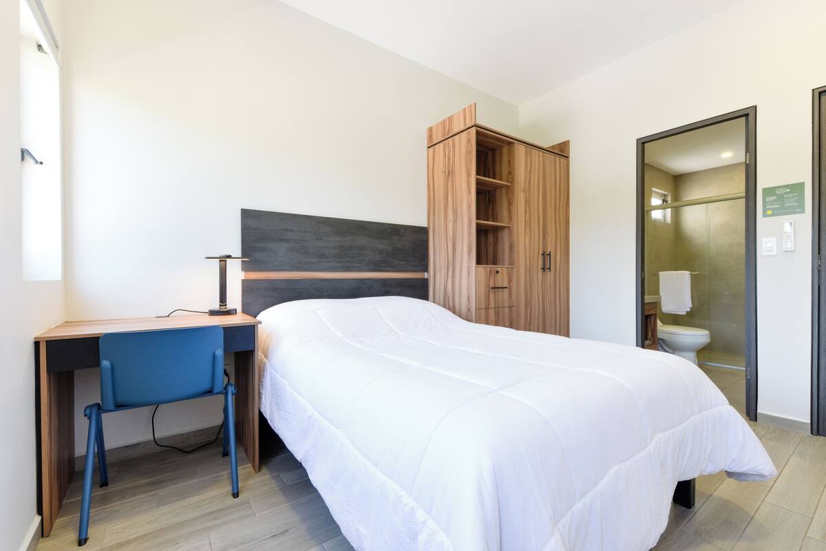 A bedroom with a bed, a desk, a chair, a wardrobe, and a bathroom.
