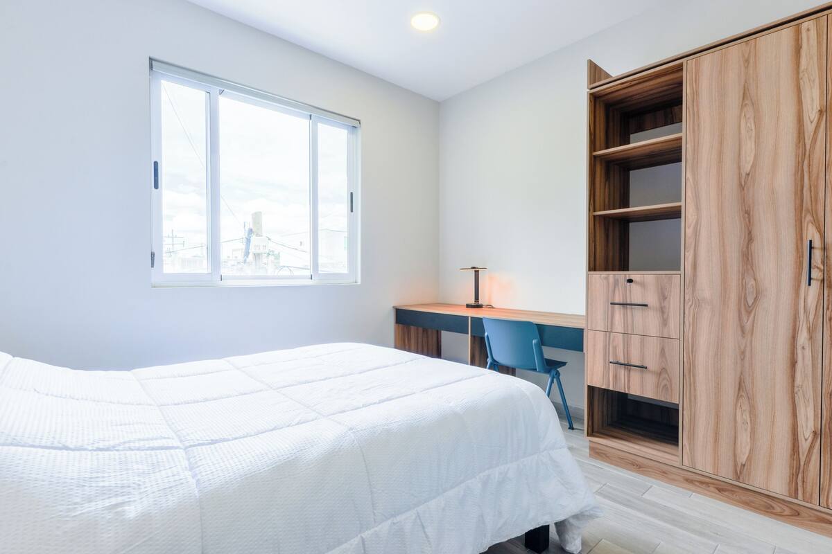 A bedroom with a bed, a desk, a chair, and a wardrobe.