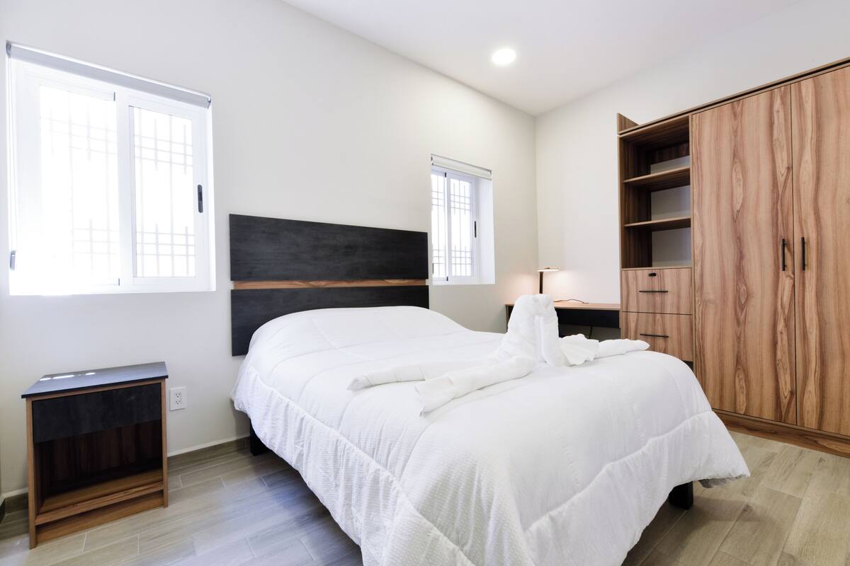 A bedroom with a bed, a wardrobe, a nightstand, and two windows.