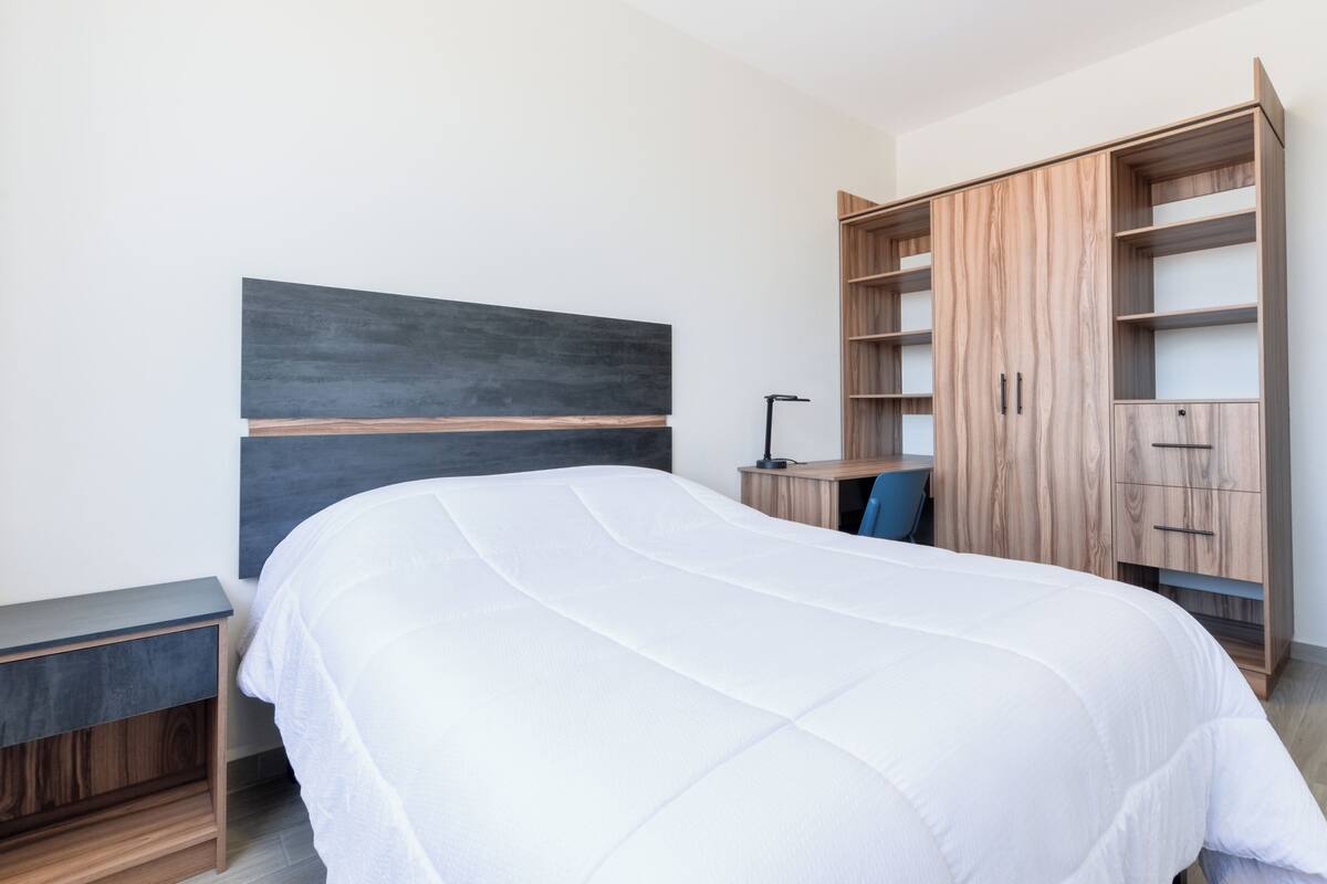 A bedroom with a bed, a nightstand, a desk, and a wardrobe.