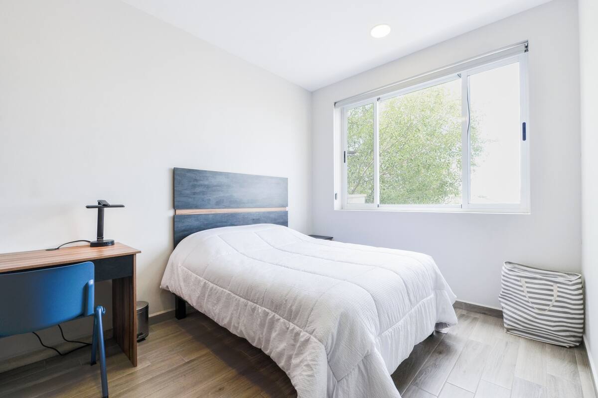 A bedroom with a bed, a desk, a chair, a window, and a radiator.