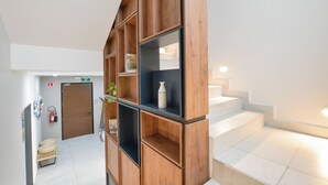 A modern hotel lobby with a wooden bookshelf, a fire extinguisher, a door, and a staircase. - Casa Curie (Monterrey)