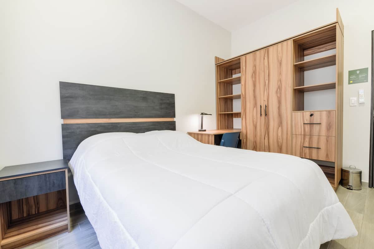 A bedroom with a bed, a desk, and a wooden wardrobe.
