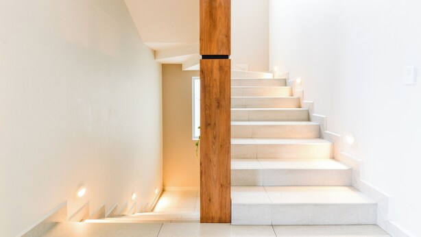 A modern staircase with a wooden column, white walls, and recessed lighting. - Casa Curie (Monterrey)