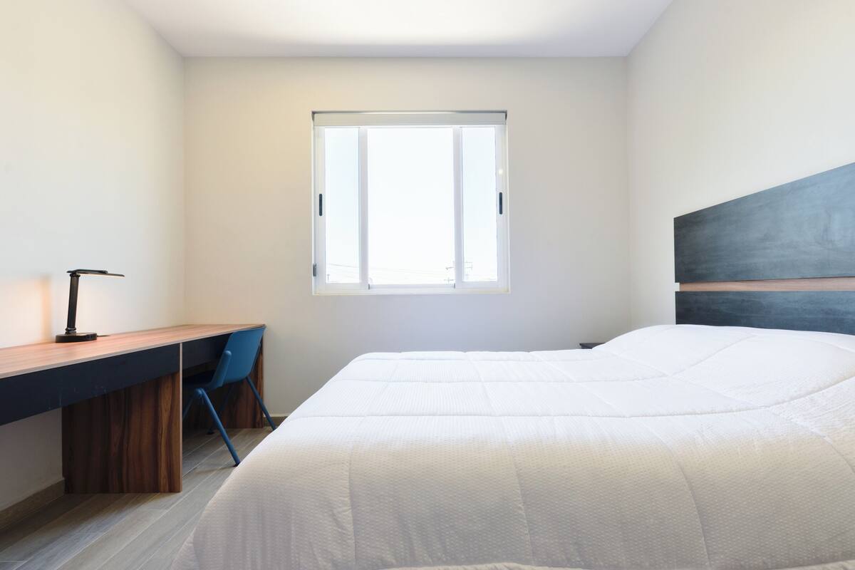 A bedroom with a bed, a desk, a chair, and a window.