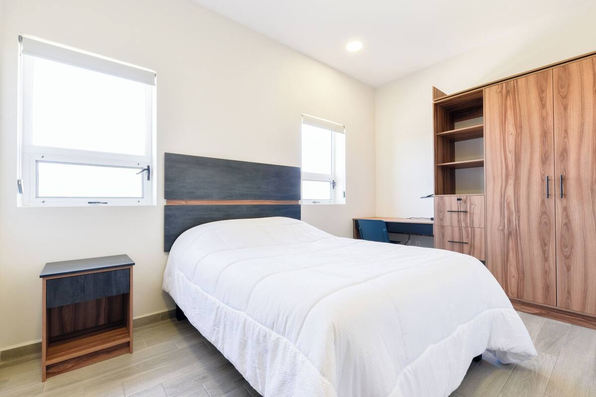 A bedroom with a bed, bedside tables, a wardrobe, and windows.