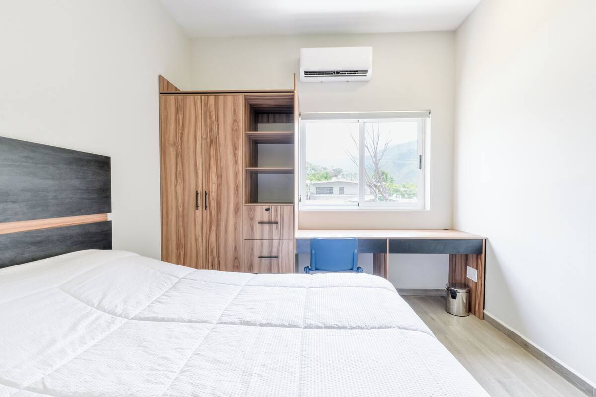 A bedroom with a bed, a desk with a chair, a wardrobe, and a window with a view.