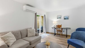 A living room with a sofa, a coffee table, a dining table with chairs, and an air conditioning unit. - L`Acadie House in the Annapolis Valley (New Minas)