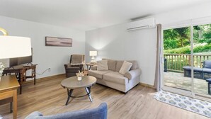 A living room with a sofa, armchair, coffee table, TV, and a view of the outdoors through a sliding glass door. - L`Acadie House in the Annapolis Valley (New Minas)