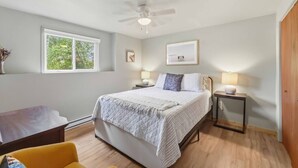A bedroom with a bed, bedside tables, a ceiling fan, a window, and a door. - L`Acadie House in the Annapolis Valley (New Minas)
