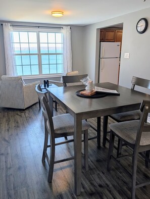 A dining area with a table, chairs, and a view of the ocean through large windows. - Harbour-View Overlooking the Bay of Fundy - Digby (Digby)