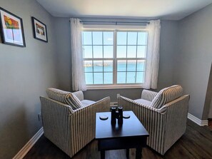 A room with two striped armchairs, a small table, and a window with a view of the sea. - Harbour-View Overlooking the Bay of Fundy - Digby (Digby)