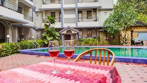 A poolside area with a table covered in a floral tablecloth, two glasses of red drink, and a chair. - Classic With Balconytownhouse Calangute (Calangute)
