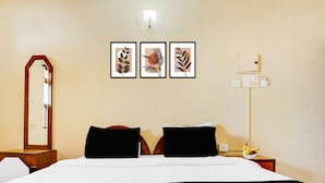 A hotel room with a large bed, two black pillows, a mirror, a bedside table with a lamp, and three framed leaf artworks on the wall. - Classic With Balconytownhouse Calangute (Calangute)