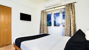 Ein Schlafzimmer mit Bett, Fernseher, einem Fenster mit Vorhängen und einer Tür.