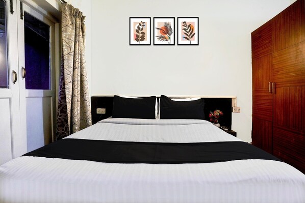 A bedroom with a bed, a wooden wardrobe, a door, and three framed pictures on the wall.