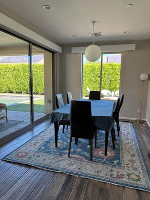 A dining area with a table, chairs, a rug, and a view of a hedge outside. - Serene Oasis in the Desert- Trilogy at the Polo Club (Indio)