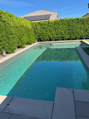A rectangular swimming pool with clear water, surrounded by a hedge and a building with a sloped roof. - Serene Oasis in the Desert- Trilogy at the Polo Club (Indio)