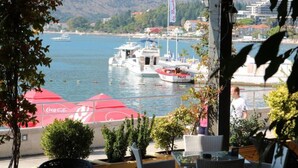 Vista sulla costa con barche, un ombrellone con marchio Coca-Cola e una persona che cammina.