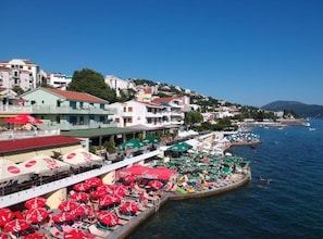 Eine Küstenstadt mit Gebäuden, einem Steg mit Sonnenschirmen und Booten auf dem Wasser.