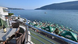 Un balcó amb mobiliari de vimet, una taula amb ampolles i gots, i una vista del mar amb vaixells i para-sols.