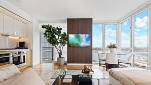 Una sala moderna con sofá, mesa de centro y zona de comedor con sillas. Cuenta con una cocina equipada y un ventanal con vistas a la ciudad.