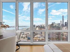 A room with large windows offering a city view, a dining table, and a sofa.