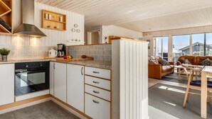 A modern kitchen with white cabinetry, a built-in oven, and a dining area with a wooden table and leather sofa. - "Danail" - 250m from the sea by Interhome (Juelsminde)