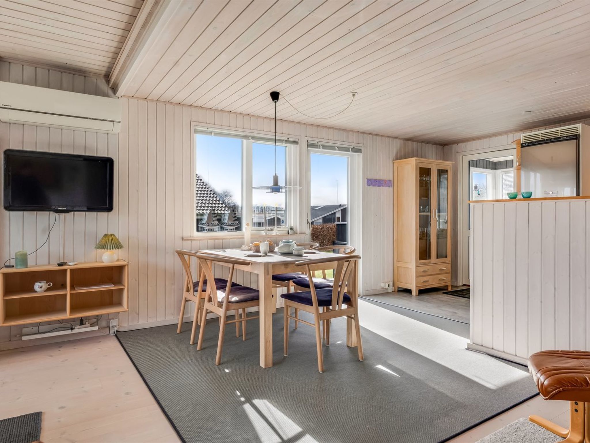 A room with a dining table, chairs, a television, a cabinet, and a window with a view of buildings.