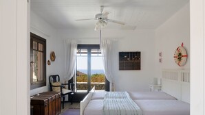 Ein Schlafzimmer mit Bett, Schreibtisch, Stuhl, einem Fenster mit Vorhängen, einem Deckenventilator und Meerblick.