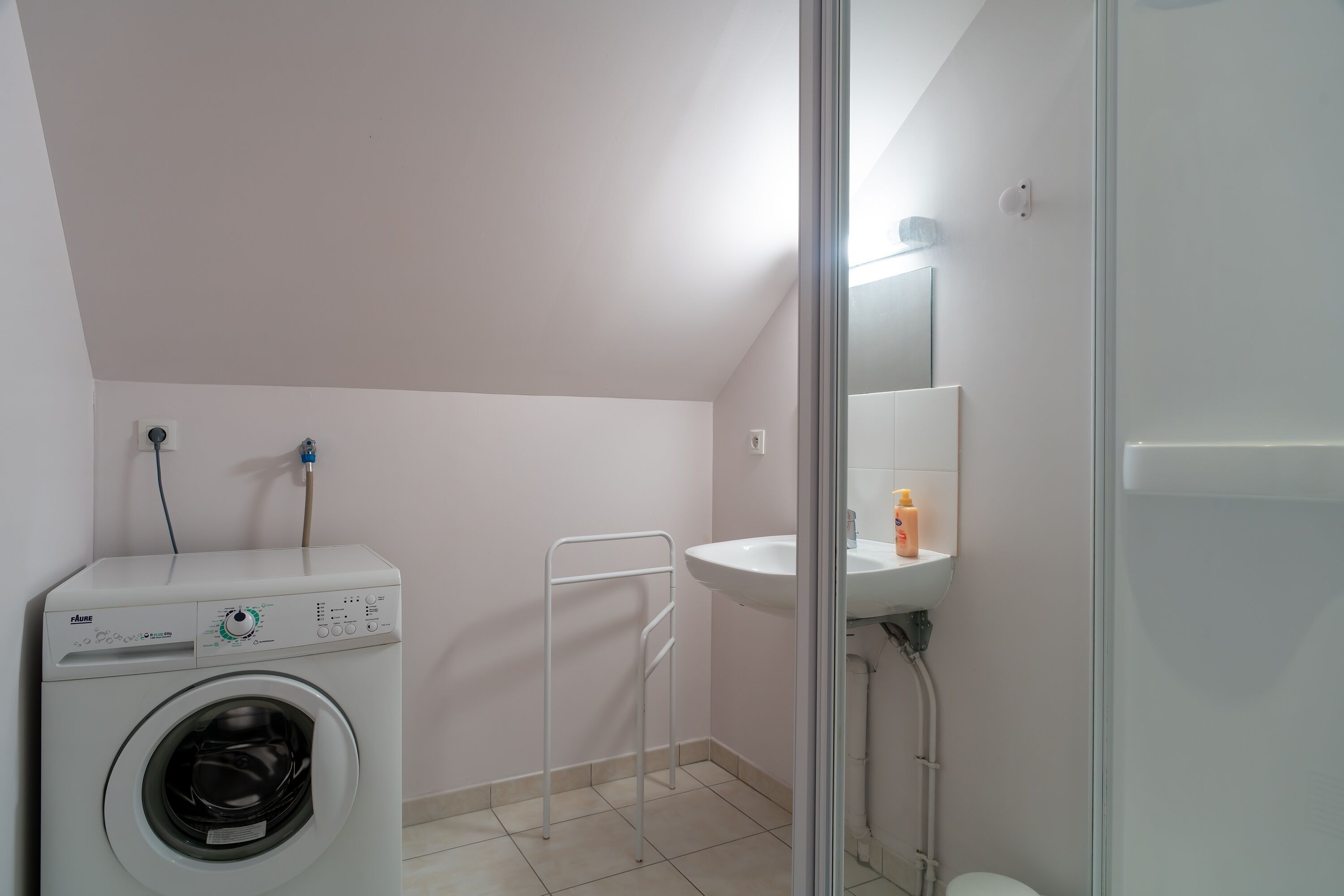 A small, clean laundry room with a washing machine, a sink, and a shower.