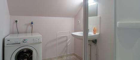 A small, clean laundry room with a washing machine, a sink, and a shower.