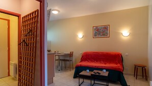 Una stanza con un letto, un tavolo, una sedia, un tavolo da pranzo con sedie, una lampada a parete e una porta.