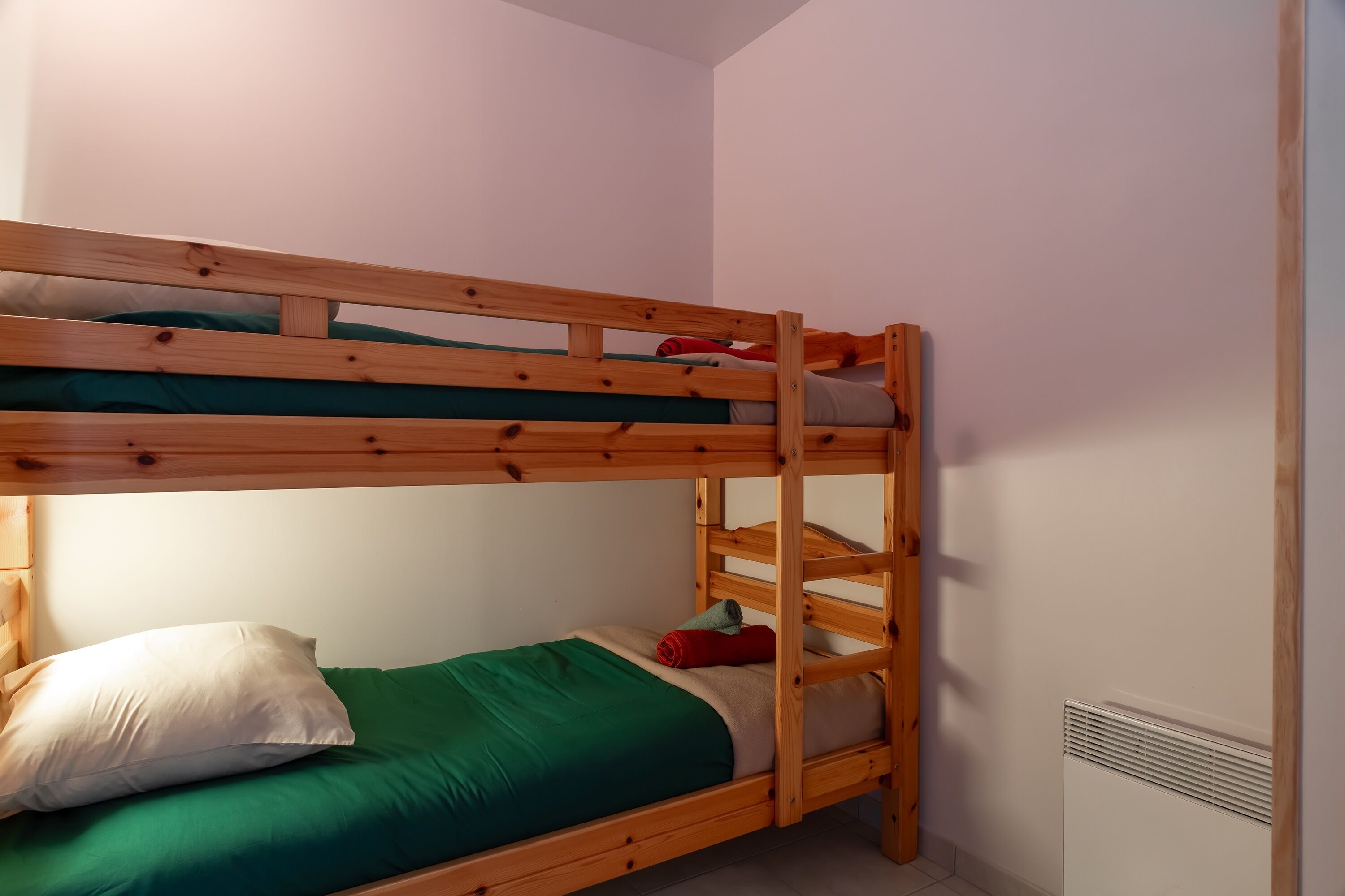 Un lit superposé avec un matelas et des oreillers verts, une tête de lit en bois et un mur blanc.