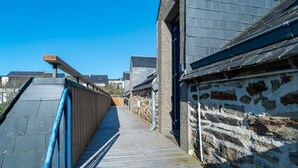 A narrow wooden pathway leading to a stone building with a sloped roof. - Les Mésanges Bleues - Au Soleil Breton (Saint-Nic)