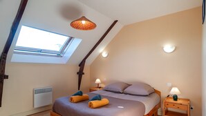 A bedroom with a sloped ceiling, a skylight, a bed with towels, bedside lamps, and a heater. - Les Mésanges Bleues - Au Soleil Breton (Saint-Nic)