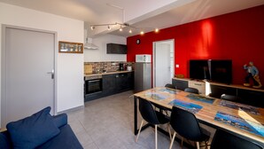 A modern kitchen with a red accent wall, a dining area with a wooden table and chairs, and a blue sofa in the foreground.