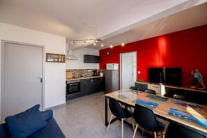 Una cocina moderna con una pared de acento roja, un área de comedor con mesa y sillas de madera, y un sofá azul en primer plano.